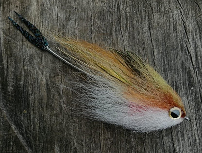 Black tail Bocon peacock bass snack fly in tan and cream with red gill and a black tail on wood. 