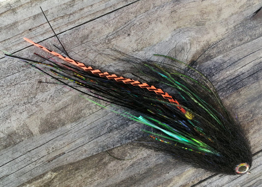 Burgundy Head hand-tied Arapaima fly in black with orange synth saddle hackle and pearl flash and a gold eye on weathered wood