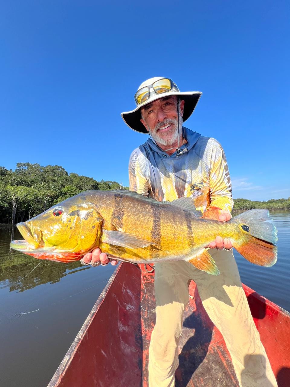 Happy angler holding a large peacock bass in a boat, caught on the Gray sabalo fly