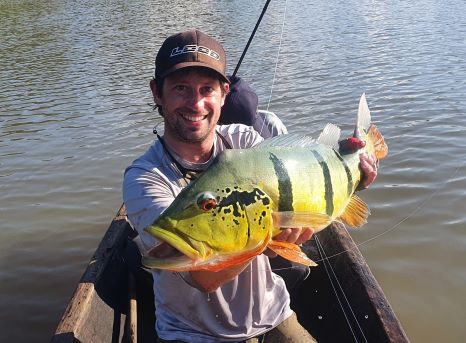 Angler holding a barred peacock bass caught on the Macaw Fly from a canoe