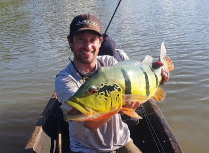 Angler holding a barred peacock bass caught on the Macaw Fly from a canoe