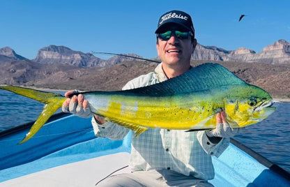 Smiling angler holding a mahi-mahi with rocky mountains behind, caught on a Gray Bait Fish Diver.