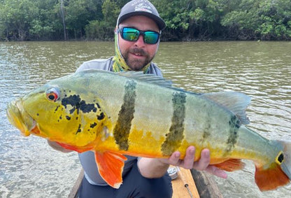 Angler with a fat barred peacock bass, caught on the Red Head fly