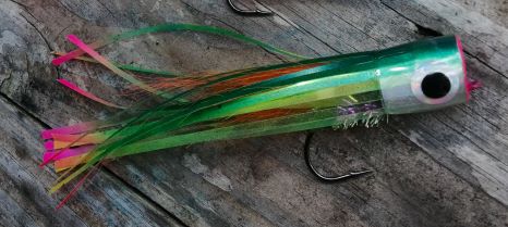 Green hand-tied popper fly with a silver head, black eye and green, orange and pink tail on weathered wood